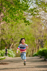 Fototapeta na wymiar 春の公園で元気で走って遊んでいる可愛い子供の様子