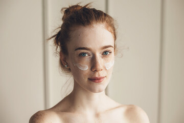 Ginger woman wearing hydrogel eye patches looking at camera with bare shoulders