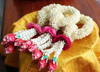 Beautiful hand-made garlands of beautiful jasmine and red roses on  gold fabric top of tray.