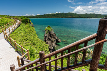 Lush maritime landscape with corals around a rock, emerald green sea, mountain and Tsukihama beach in the background. View from the top of the lookout stairs. Wooden path to contemplate the landscape.
