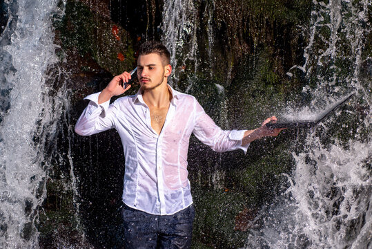 Businessman standing with waterfall with waterproof devices with IP68 water resistant protection. Attractive man in suit holding gadgets at waterfall background. - Powered by Adobe