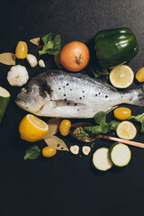 fish with lemon and vegetables. Delicious fresh fish on black dark background. Fish with aromatic herbs, spices and vegetables on a black table. healthy food, diet, cooking concept. Prepare fish