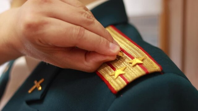 The hand removes the stars from the shoulder straps of the soldier.