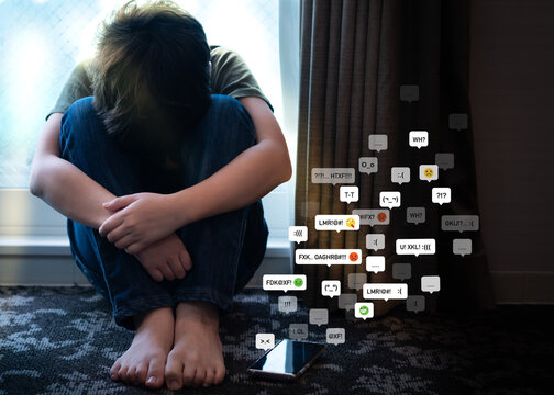 Cyberbullying - social media harassment concept. Young asian preteen, teenager boy sitting alone in the room feeling frustrated after reading bad comments. Text emoticons, Teen mental health, Online.