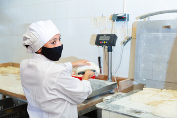 Naklejka na ściany i meble Young latin american woman working in bakery, preparing portioned pieces of dough for baking