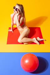 Slender woman in bikini sitting on floor in studio