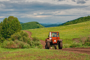 Naklejka premium Tractor agricultural machinery among fields and mountains driving along the road, Charysh