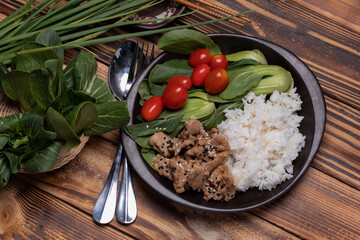 Teriyaki pork sprinkled with sesame and vegetables and steamed rice on a black plate.