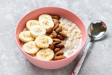 oatmeal with banana, almonds nuts in pink bowl, glass of milk, napkin on gray concrete background Top view Healthy breakfast or lunch Natural ingredients Rustic style