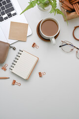 Above view of female workplace with coffee cup, laptop computer and stationery on white desk.