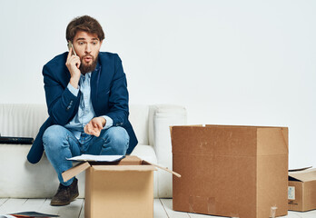 man talking on the phone sitting on the couch boxes with things moving unpacking