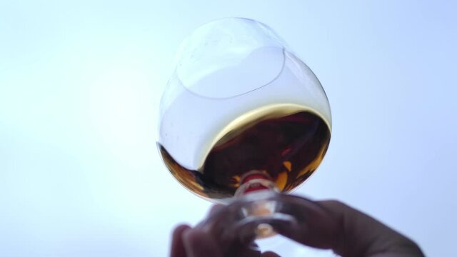 Man's hand stir slowly cognac in the glass, slow motion.  