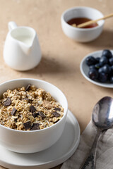 Muesli with chocolate in white bowl served with blueberry, honey and milk .