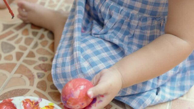 Hands of toddler little girl sitting painting colorful eggs for Easter hunt at home, Easter day holiday concept
