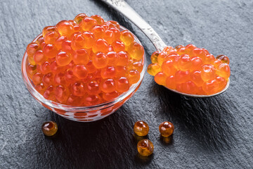 Red caviar in the bowl on gray graphite background.