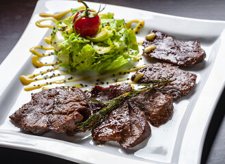 Roasted beef steaks with salad leaves on the white plate.