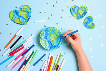 Female hand draws planet Earth with multicolored felt-tip pens on on a blue background. Science,...