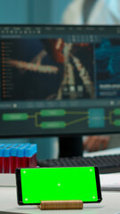 Microbiologist bringing blood samples in modern lab putting them near smartphone working with green chroma key screen placed on desk. Team of biotechnology scientists developing drugs in background