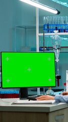 Biochemist sitting at workplace in laboratory using green mock-up screen personal computer with chroma key monitor. coworker working in background of pharmaceutical research centre.