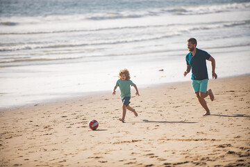 Father and son play soccer or football on the beach on summer family holidays. Dad and child playing outdoor.