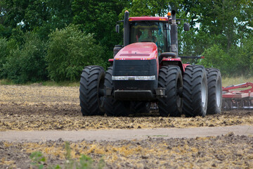 Obraz premium Red tractor with a plow on an agricultural field. work in the field with a big red tractor close-up, harvesting, farming. august 2020 Ukraine, Kiev region