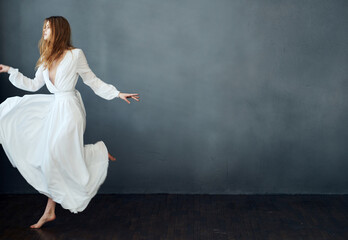 A woman in a white dress is dancing on a gray background in full growth red hair model