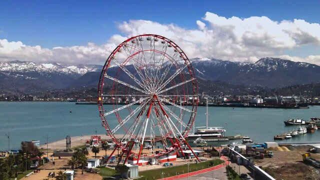Dolly zoom. Parallax effect. Drone footage ferris wheel on embankment and amazing mountain scenery 