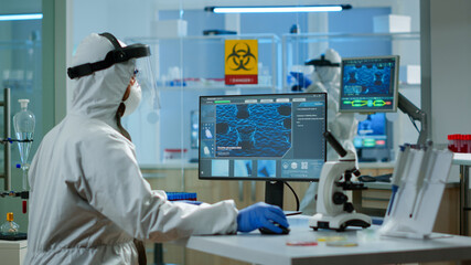 Man scientist working at vaccine development typing on pc in coverall in modern laboratory. Team examining virus evolution in medical lab using high tech, chemistry tools for scientific research.