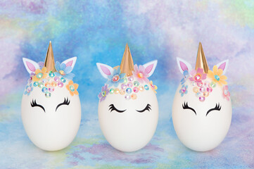 Unicorn eggs in a row. Three Easter eggs in the form of a unicorn with golden corn and flowers on mulicolor blue background. 