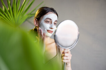 Portrait of a woman in cleansing mask and palm leaves on the background