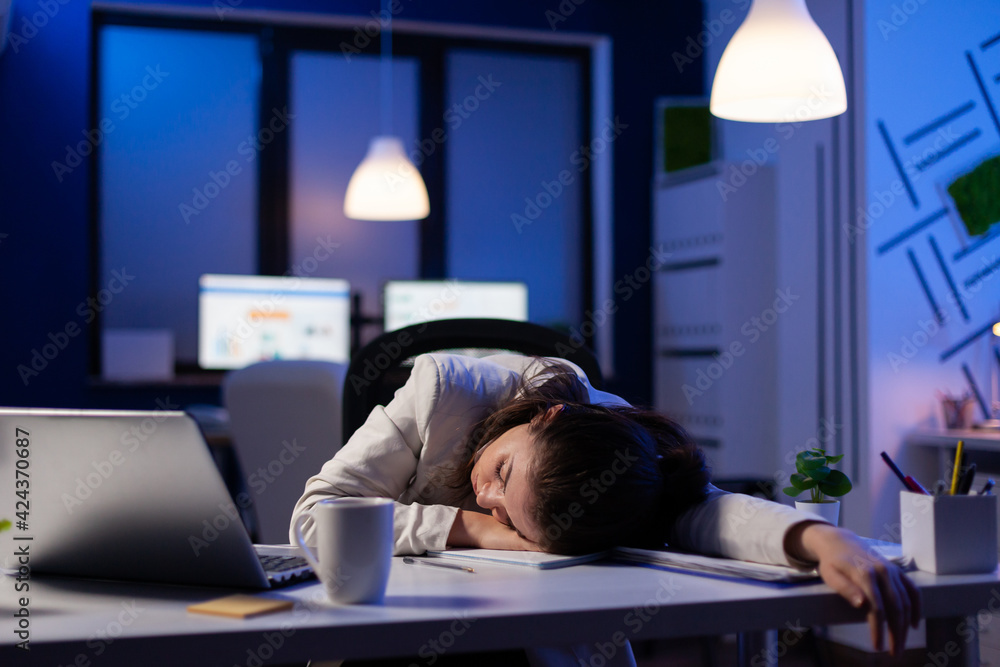 Poster entrepreneur working overtime on marketing project, falling asleep on desk while looking at financia
