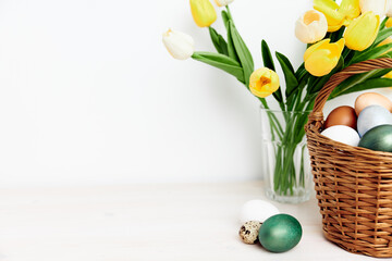 multicolored eggs in wooden baskets and yellow tulips in a vase on a light background