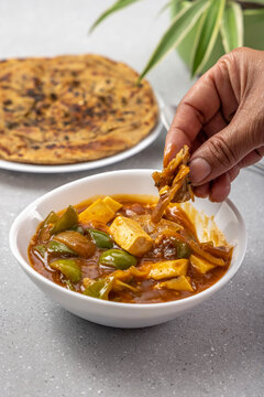 woman taking a bite of Spicy Paneer or chilli paneer or paneer tikka with capsicum, onion with lachha paratha served for meal