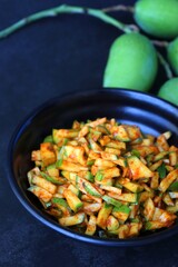 Green mango salad. Raw mango instant pickle. also known as kairichi koshimbir in Marathi. copy space over black background. Chopped raw green mangos mixed with salt, red chilli powder and sugar. 