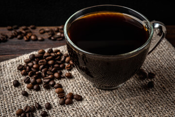 Cup of coffee with coffee beans on dark wooden background.