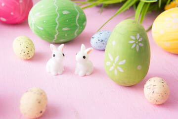 Composition with Easter eggs with rabbits or hare toys and flowers on pink wooden background