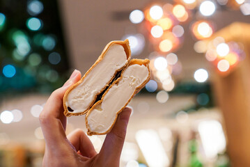 Vanilla ice cream sandwich. Hand holding a crispy wafer stuffed with vanilla ice cream. light bokeh background.
