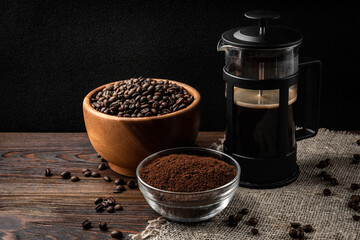 Coffee in french press, coffee beans and powder on dark wooden background.