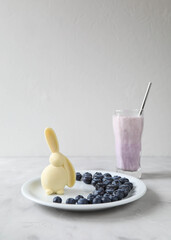 An Easter chocolate bunny in blueberry berries on a plate with a drink of milk and berries in the background is an example of an Easter breakfast for a child and the whole family