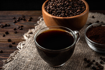 Cup of coffee with coffee beans and powder on dark wooden background
