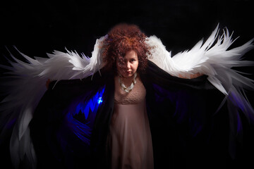 A brunette curly girl in black dress looking like an evil angel with white wings on a black...