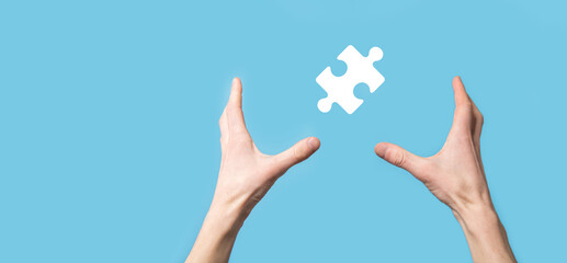 Male hand holding puzzle icon on blue background. pieces representing the merging of two companies or joint venture, partnership, Mergers and acquisition concept.