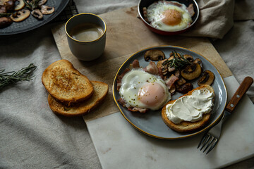 Breakfast with fried egg(sunny side up) with bacon, grilled with rosemary mushrooms and toast with cream cheese. 