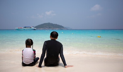 A young girl in flower-patterned clothing sat in the sand with her brother at the beach. A sea with a beautiful sky, a blue sea.