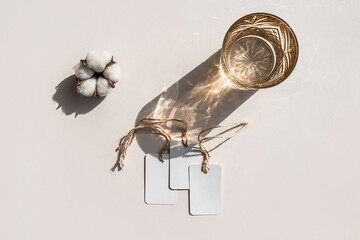Still life scene with cotton flower on beige background in sunlight and blank white tags mockup.