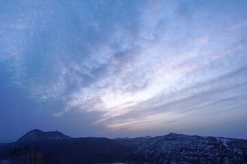 薄い雲の広がる夜明けの空と山間の湖。日本の北海道の摩周湖。