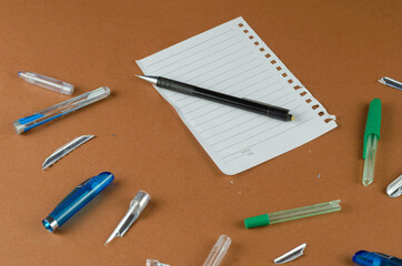Broken pens and blank sheet of paper on brown table.