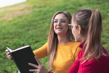 Two women enjoying reading a book in a park