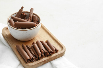 Bowl with delicious chocolate curls on light background