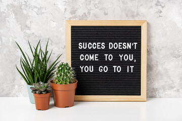 Success doesn't come to you, you go to it. Motivational quote on letter board, cactus, succulent flower on white table. Concept inspirational quote of the day. Front view